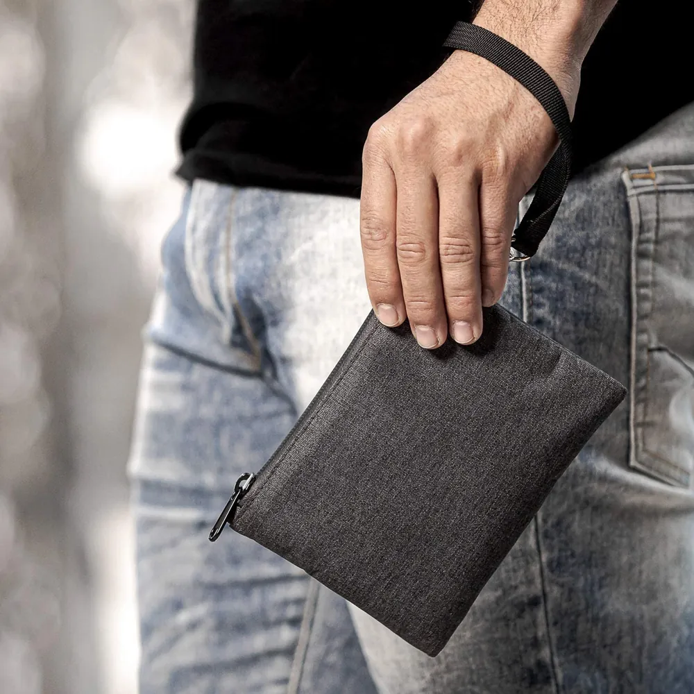 Gray zip pouch carried by its wrist strap beside the user